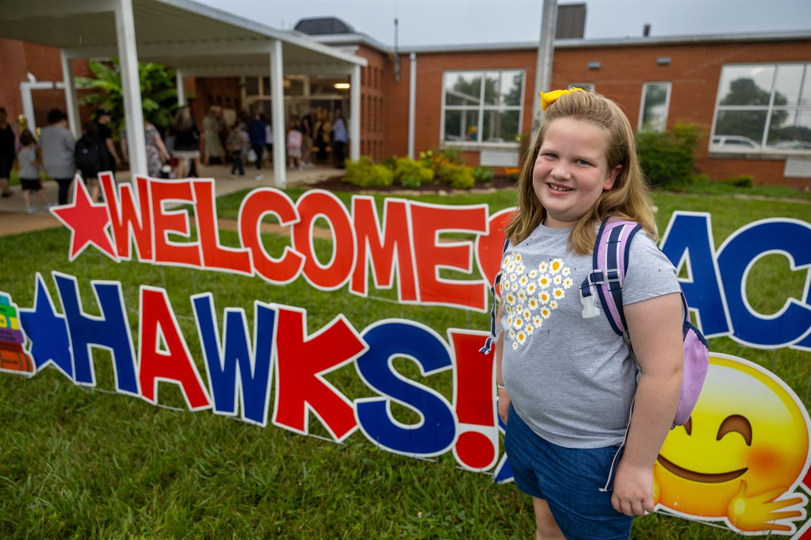 girl smiling in front of welcome hawks sign